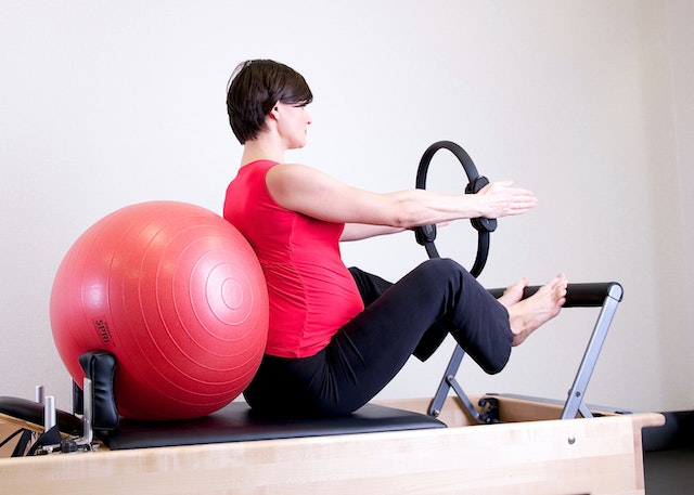 woman in red top leaning on red stability ball on a reformer
